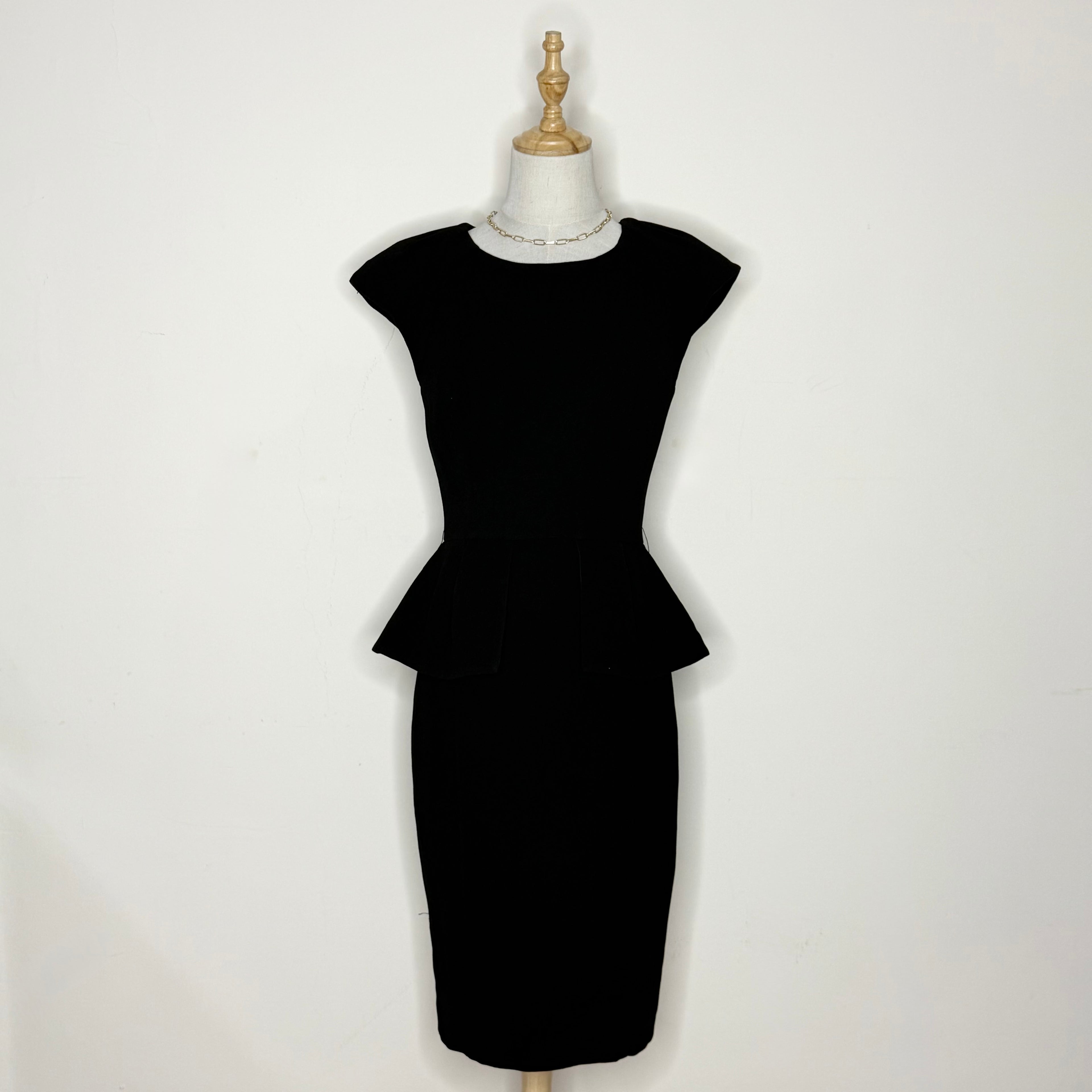 Black peplum dress on a mannequin against a white background