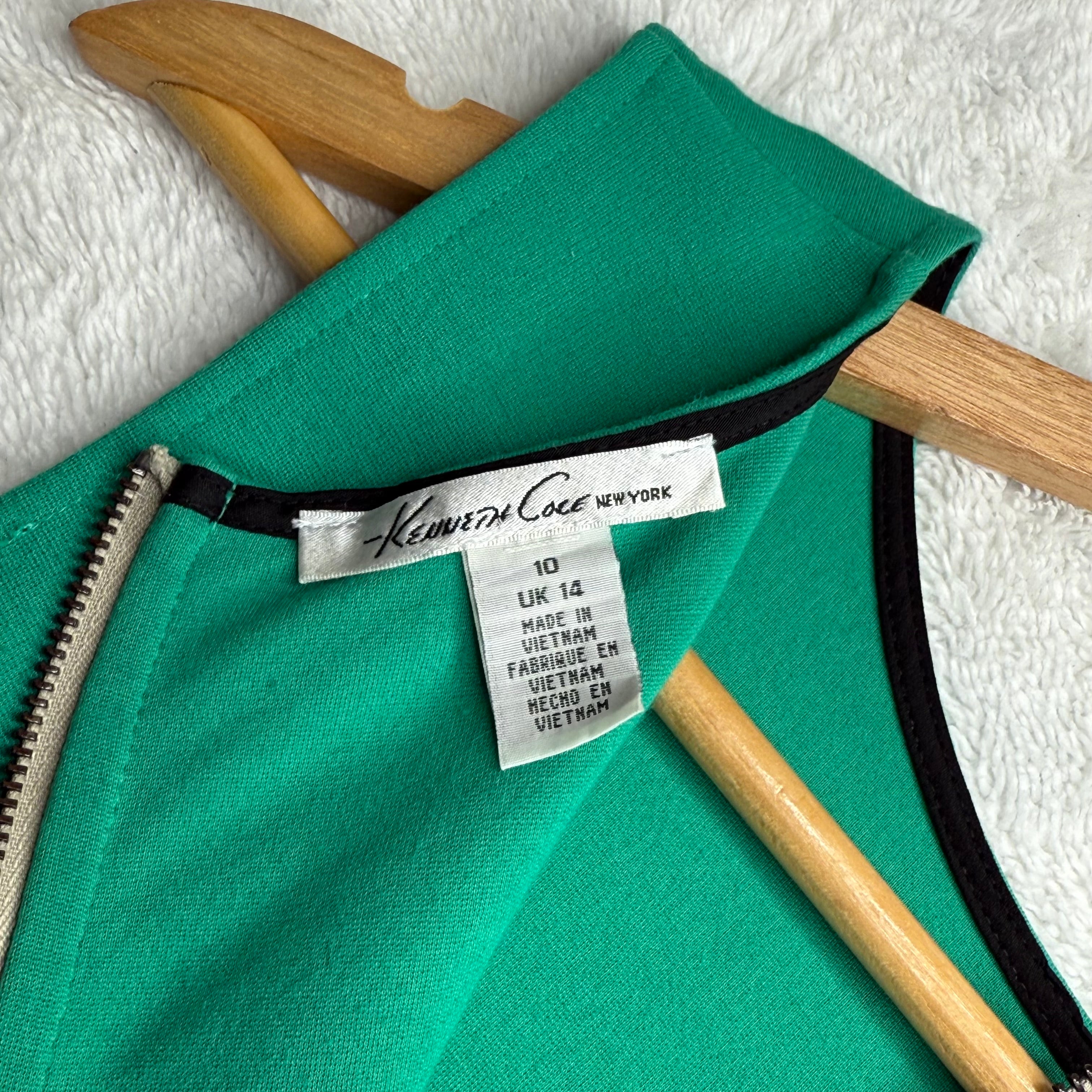 Green garment with a Kenneth Cole label on a wooden hanger against a white background